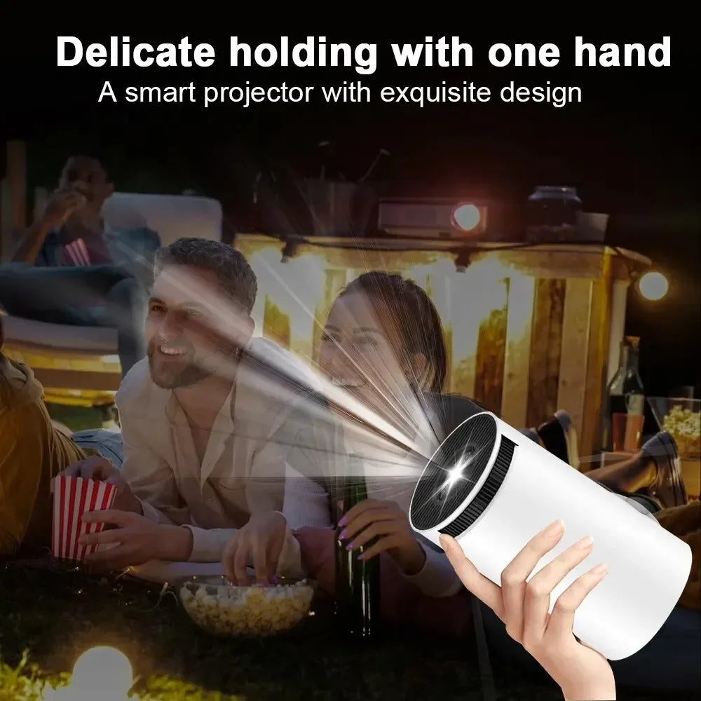 Cinemaster Pro 4k Smart Projector held by a hand with people enjoying a movie outdoors.