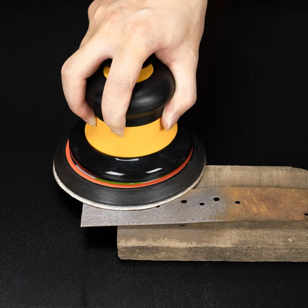 Hand using a Glissedi Palm Sander on a wooden surface with a black background