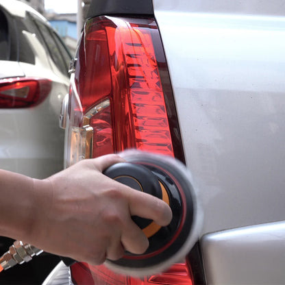 Person applying a black and orange circular object to a car's red tail light.