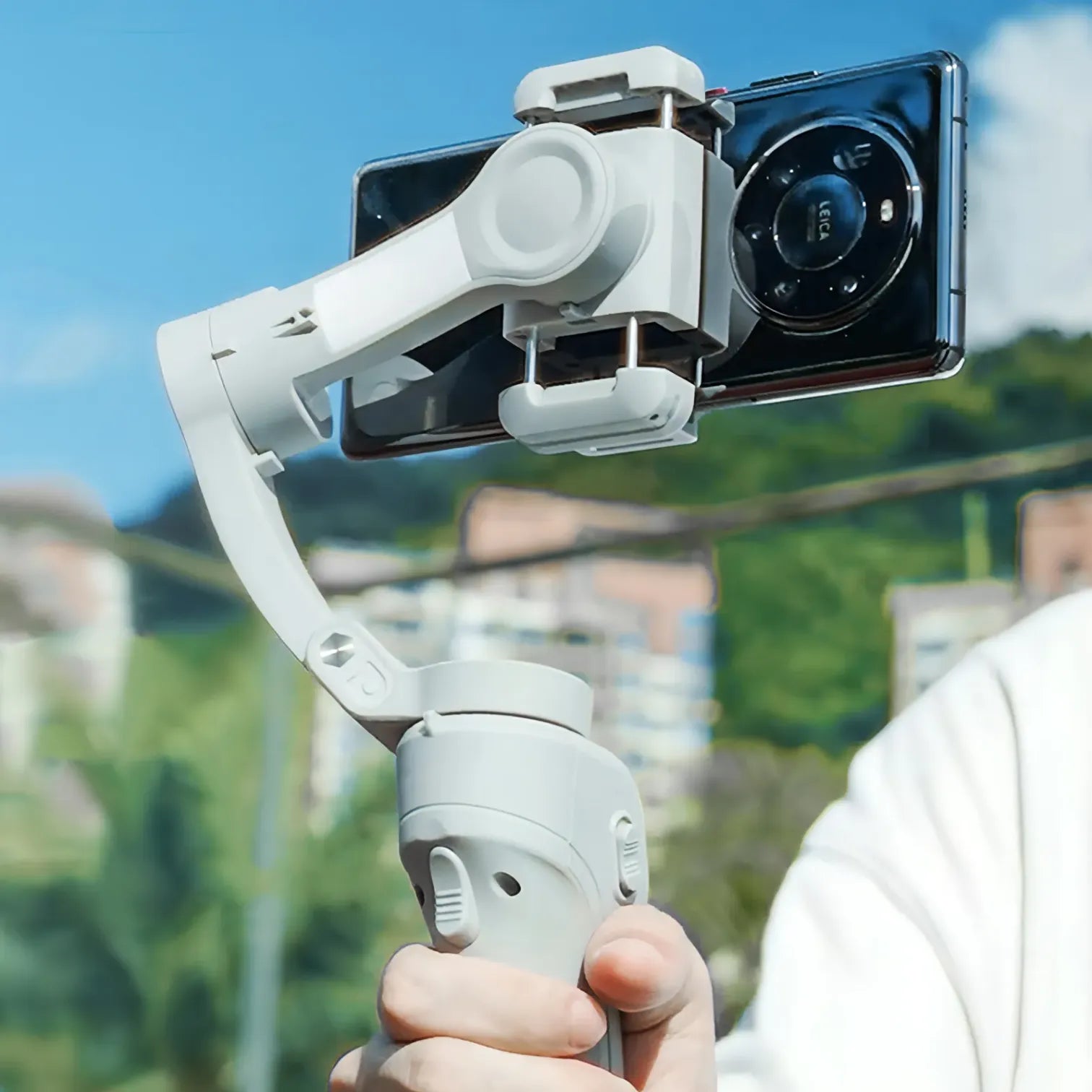 Hand holding a smartphone Puruxe Gimbal with a clear sky and blurred background