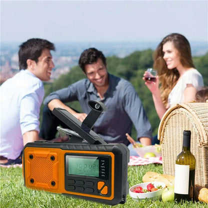Portable SafeNetto Emergency Radio with orange and black design on a grassy field with people enjoying a picnic.