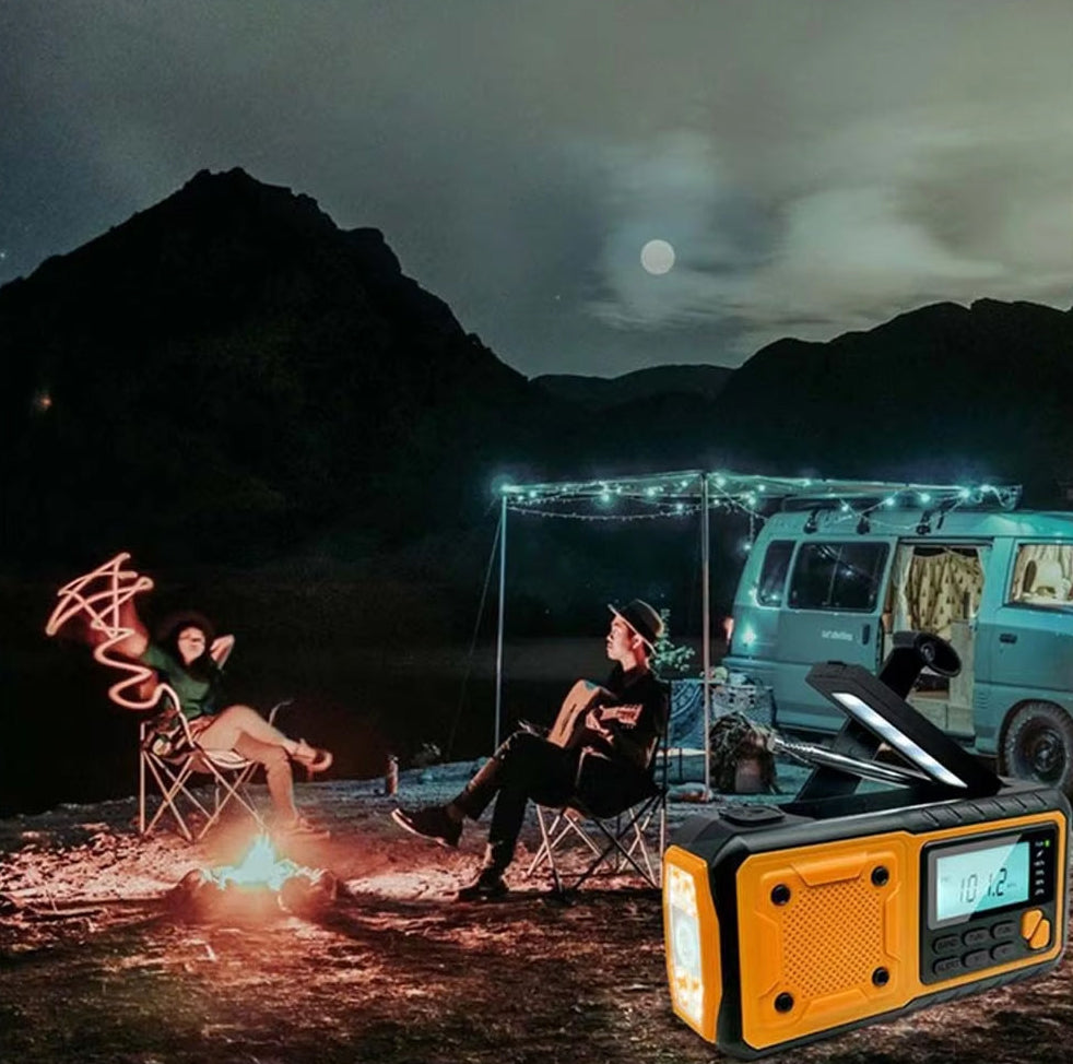 Two people sitting by a campfire at night with a van in the background, featuring a portable SafeNetto Emergency Radio in the foreground.
